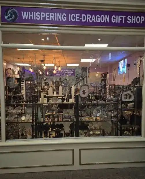 Purple sign with white lettering reading ’whispering ice-dragon gift shop’ above a glass storefront displaying various decorative items.